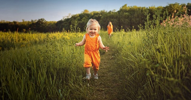 Lapsi juoksee kohti kameraa oranssissa haalarissa.