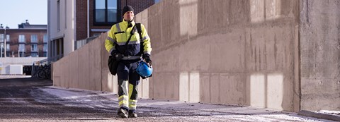 Oulun Energian työntekijä kävelee työvarustuksessa kerrostalon edessä hiekoitetulla tiellä.