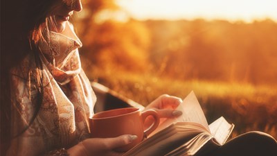 A woman reading a book with a cup of coffee in her hand.