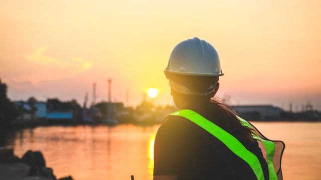 Kypäräpäinen henkilö katselee kaunista auringon laskua.