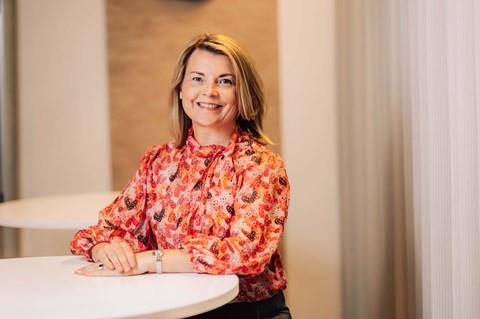 Responsibility Director Katja Virkkunen smiles and leans on the white table.