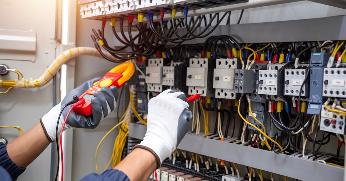 An electrical worker measuring with a meter, only the worker's hands are visible in the picture.