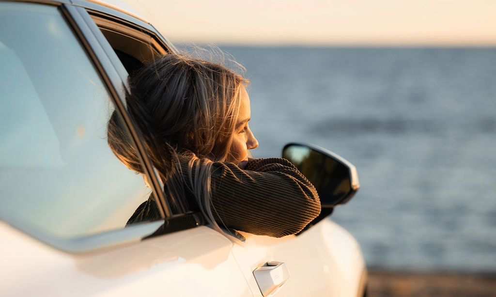 A young woman leans out of a car window on a summer evening. Bay of Bothnia can be seen in the background.