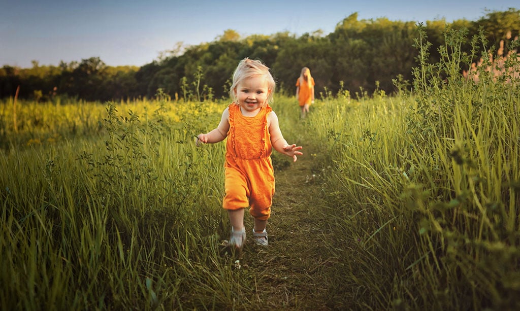 A child wearing an orange overall runs towards the camera.