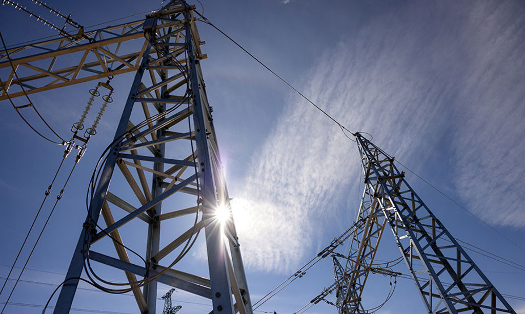 The bright sun shines behind the poles of the power plant.