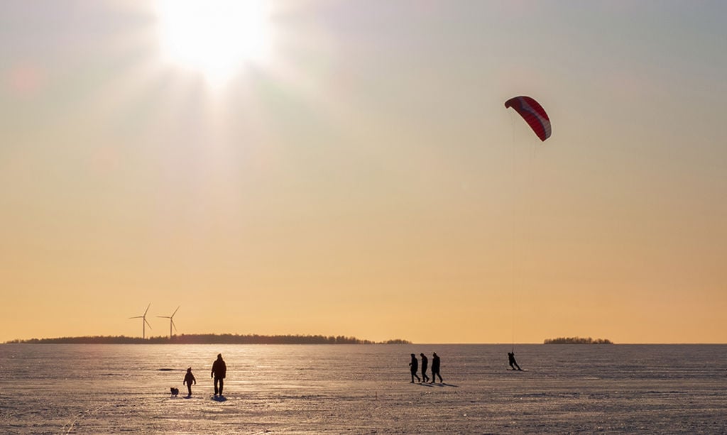 People are walking on the icy sea. Two wind turbines behind.