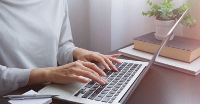 A woman's hands typing on a laptop keyboard.