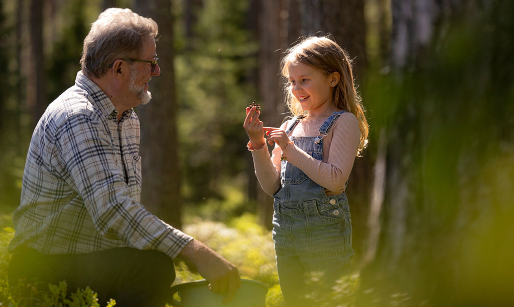 A young girl shows her grandfather a small cone she found in the forest.