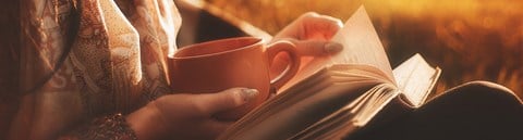 The woman is holding a coffee cup and a book in the autumn sunshine.