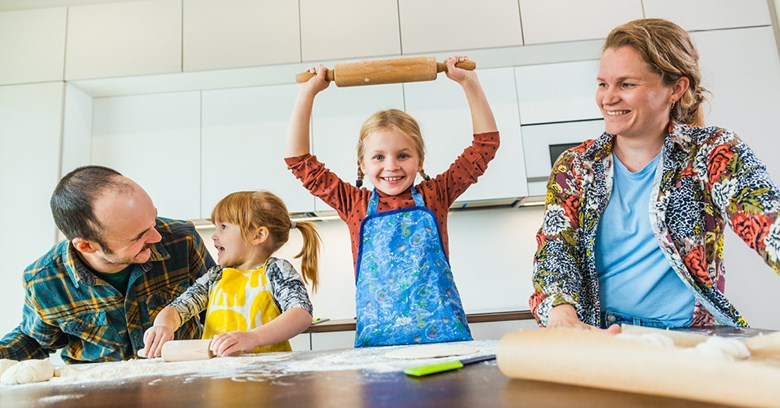 A family of four baking together in the kitchen of their home.