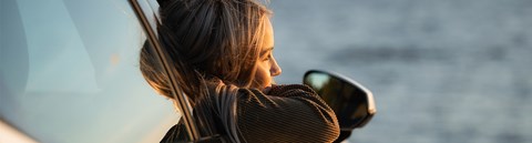 A young woman leans out of a car window on a summer evening.