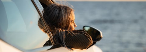 A young woman leans out of a car window on a summer evening at the seaside.