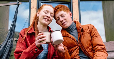 Red-haired young woman and red-haired young man are sitting on stairs and holding teacups.