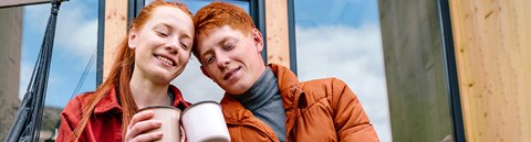 Young man and young woman are sitting on stairs and holding their coffeemugs.