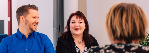 A man and two women are sitting across a table, the other woman is not facing the camera. They are having a good time.