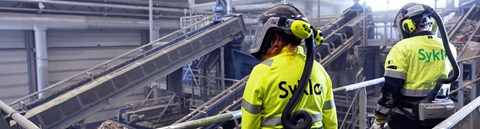 Two Syklo's employees are facing away from camera and are monitoring sorting line's activities infront of them.