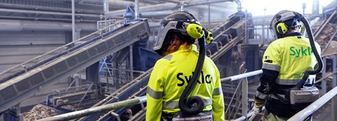 Two Syklo's employees are in waste sorting factory monitoring sorting line operations.