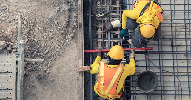 Rakennustyömaalla valetaan betonia. Työntekijät ovat turvavaatteissa.