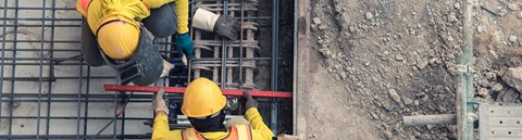 Two construction workers are in work clothes, pouring cement into buildings.