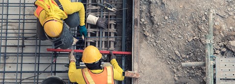 Two construction workers are in work clothes, pouring cement into buildings at a construction site.