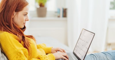 Punatukkainen nainen istuu ja selaa sylissään olevaa kannettavaa tietokonetta.