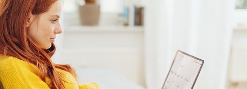 Red-haired woman is sitting and going through her laptop.