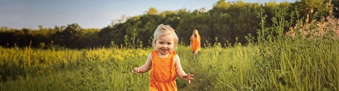 A happy todler is running on a field towards the camera. 