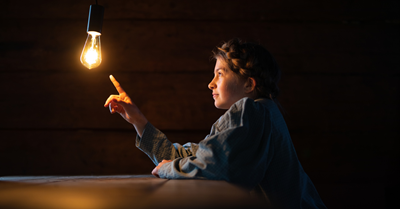 Lamppu roikkuu katosta ja istuva tyttö tuijottaa lamppua.