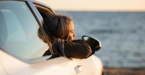 Girl is sitting in a car with an open window and looking to the sea.