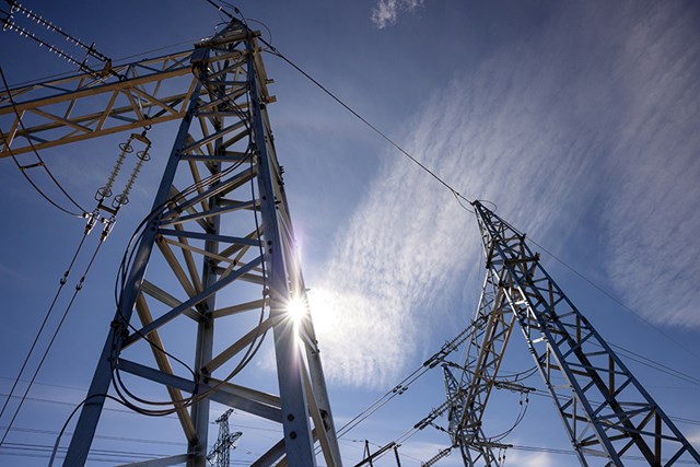 The bright sun shines behind the poles of the power plant.