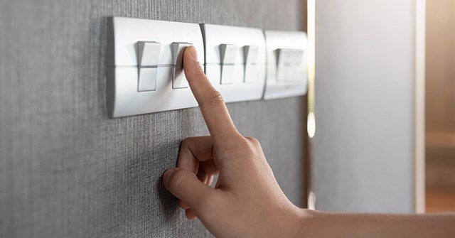 A finger on a light switch. Energy is saved by reducing lighting.