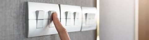 A finger on a light switch. Energy is saved for example by  reducing lighting.