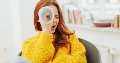 A red-haired woman in a yellow sweater is sitting and looking to the camera through a paper roll.