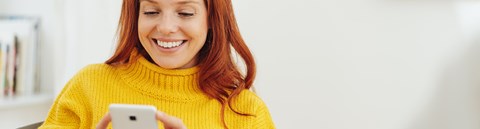 A smiling woman is scrolling through her phone.