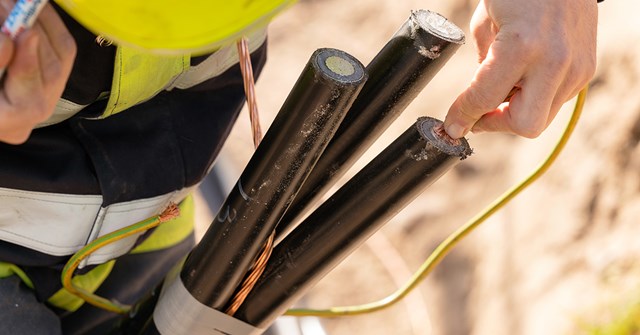Oulun Energian työntekijä pitelee käsissään mustia sähkökaapeleita.