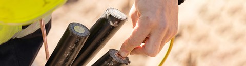 An employee of Oulu Energy is holding three black electronical cables in their hands.