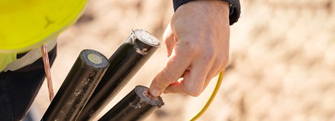 An employee of Oulu Energy is holding a copper wire on top of electronical cables.