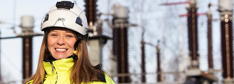 An employee of Oulu Energy is wearing work gear and smiling to the camera.
