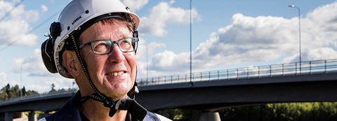 An employee of Oulu Energy is looking up. He is wearing a helmet and standing in front of the Oulu river.
