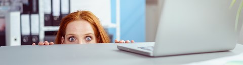 A red-haired woman is peaking carefully behind a desk.