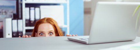 Woman is peeking behind a work desk.