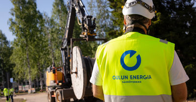 Oulun Energian työntekijä seisoo selin kameran edessä. Taustalla näkyy kaivinkone.