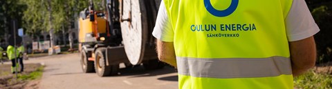 An employee of Oulu Energia Sähköverkko Oy, standing with his back to the camera, looks at the excavator in front of him.