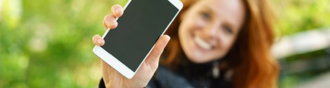 A happy woman is sitting on a park bench and holding her phone closer to the camera.