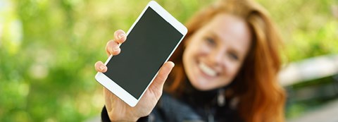 A woman is sitting on a park bench and holds her phone close to the camera.