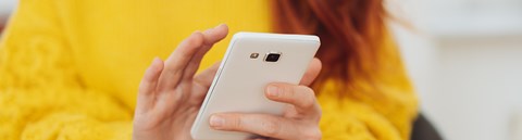 A woman wearing a yellow sweater is scrolling her smartphone.