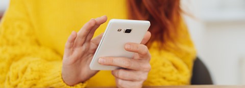 A woman is scrolling her smartphone. She is wearing a yellow shirt.