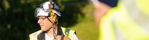 An employee of Oulu Energy is wearing their work gear. There is an iron chain in front of him.