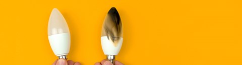In front of an orange background a person is holding two light bulbs.