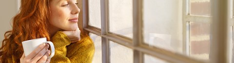 A red-haired woman sits on the windowsill and looks outside.